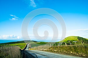 The stunning landscape of the way in a rural area in New Zealand. Gravel road among green grassland with blue sky. I