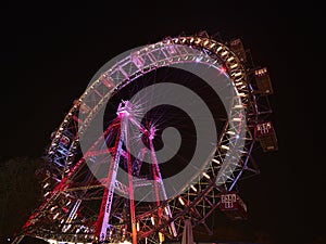 Stunning low angle view of popular Ferris wheel with colorful rim at night in amusement park Prater in Vienna, Austria.