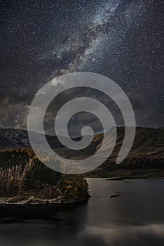 Stunning majestic digital composite landscape of Milky Way over Hawes Water in Lake District