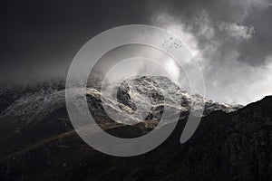 Stunning moody dramatic Winter landscape image of snowcapped Tryfan mountain in Snowdonia with stormy weather brooding overhead