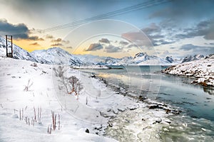 Stunning morning view of Torsfjorden fjord with cracked ice and snowy mountain peaks at background