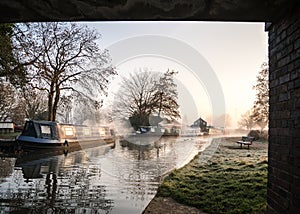 Stunning old canal house boats landscape under bridge sunrise in countryside with river and single lone wooden bench frost photo