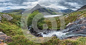 Stunning panorama landscape image of stream flowing over rocks near Llyn Ogwen in Snowdonia during eary Autumn with Tryfan in