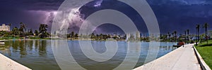 A stunning panoramic shot of a vast rippling lake surrounded by lush green palm trees, grass and plants with powerful storm clouds