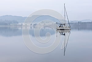 Stunning peaceful landscape image of misty Spring morning over Windermere in Lake District and distant misty peaks
