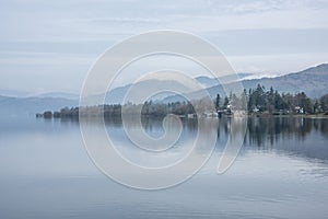 Stunning peaceful landscape image of misty Spring morning over Windermere in Lake District and distant misty peaks