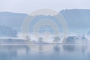 Stunning peaceful landscape image of misty Spring morning over Windermere in Lake District and distant misty peaks