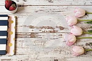 Stunning pink tulips, stripe notebooks and strawberries on white light rustic wooden background. Copy space, floral frame. Wedding