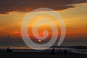 A stunning red and yellow sunrise over the vast ocean with waves rolling into the shore and people on the beach in Carolina Beach