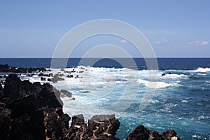 Stunning shades of blue of the Pacific Ocean contrasted against a black volcanic rocky shoreline at Paupahoehoe Point