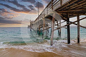 A stunning shot of the Balboa Pier at sunset with powerful clouds, vast blue ocean water and waves crashing into the pier