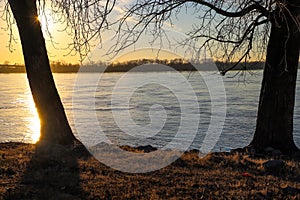 A stunning shot of the blue running waters of the Mississippi river with bare trees and brown and yellow grass along the banks