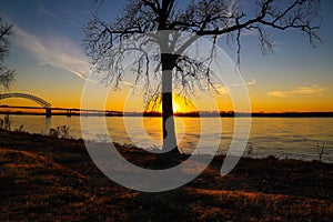 A stunning shot of a gorgeous red, blue and yellow sunset over the Mississippi river with bare winter trees along the banks