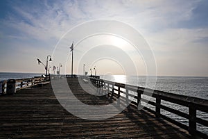 A stunning shot of a long brown wooden pier at sunset with vast blue ocean water and American flags on curved light posts