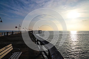 A stunning shot of a long brown wooden pier at sunset with vast blue ocean water and American flags on curved light posts