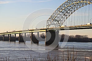 A stunning shot of a long metal bridge over the Mississippi river at sunset with cars and semi trucks