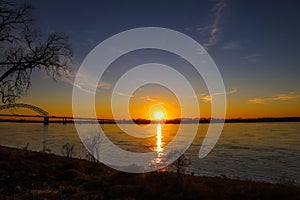 A stunning shot of a long metal bridge over the Mississippi river at sunset with a gorgeous blue, yellow and orange sky