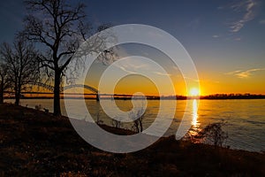 A stunning shot of a long metal bridge over the Mississippi river at sunset with a gorgeous blue, yellow and orange sky