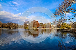 A stunning shot of the still blue waters of the lake in the park surrounded by gorgeous autumn colored trees