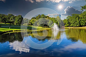 A stunning shot of still silky brown lake with a water fountain in the middle of the lake surrounded by green grass