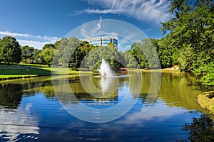 A stunning shot of still silky brown lake with a water fountain in the middle of the lake surrounded by green grass