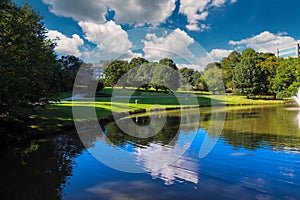 A stunning shot of still silky brown lake with a water fountain in the middle of the lake surrounded by green grass