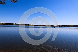 A stunning shot of the vast deep blue lake water with lush green and autumn colored trees across the lake