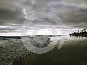 a stunning shot of the waves rolling into the beach with smooth sand and powerful storm clouds