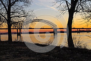 A stunning shot of a white motor boat sailing down the Mississippi river with a gorgeous yellow and red sunset with trees