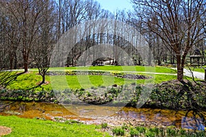 A stunning spring landscape in the garden with a flowing river surrounded by lush green grass, bare winter trees