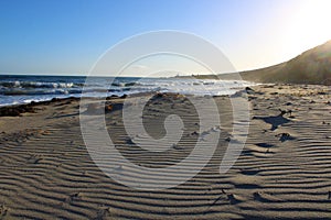 A stunning summer landscape at the beach at sunset with blue ocean water and waves rolling into the silky brown sands of the beach