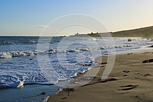 A stunning summer landscape at the beach at sunset with blue ocean water and waves rolling into the silky brown sands of the beach