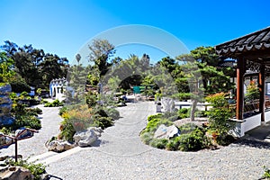 A stunning summer landscape in a Japanese garden with lush green trees and plants with brown buildings and clear blue sky