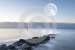 Stunning sunrise landscape over rocks in sea with super moon