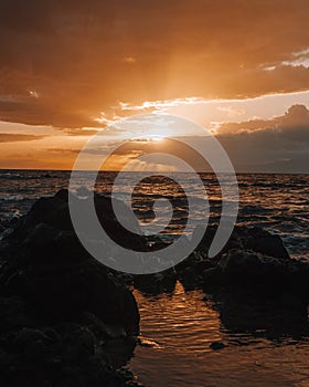 Stunning sunset over a rocky beach shoreline, with the glistening ocean waters in the background