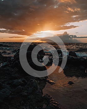 Stunning sunset over a rocky beach shoreline, with the glistening ocean waters in the background