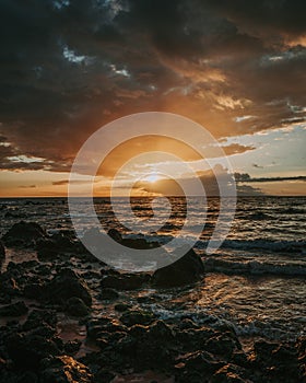 Stunning sunset over a rocky beach shoreline, with the glistening ocean waters in the background