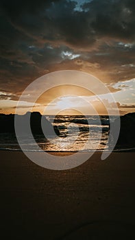 Stunning sunset over a rocky beach shoreline, with the glistening ocean waters in the background