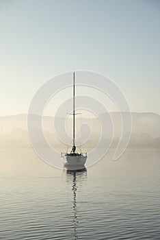 Stunning unplugged fine art landscape image of sailing yacht sitting still in calm lake water in Lake District during peaceful