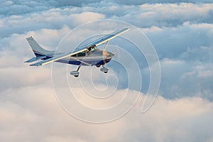 Stunning view of a blue and white little private Cessna airplane browsing the sky over fluffy fairy tale clouds.