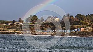 Stunning view of a vibrant rainbow arching over a row of houses located near a tranquil coastline