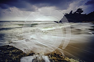 Stunning white wave flow hitting the sandy beach with dark cloud