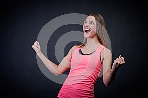 Stunning woman in sports uniform on an isolated black background keeps her fists from happiness, showing victory