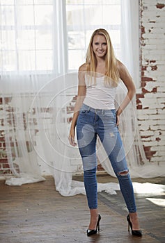 Stunning young blonde girl poses in studio wearing tank-top and blue jeans