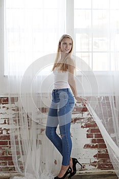 Stunning young blonde girl poses in studio wearing tank-top and blue jeans