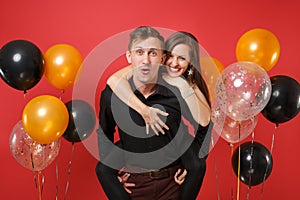 Stunning young couple in black clothes celebrating birthday holiday party on bright red background air balloons