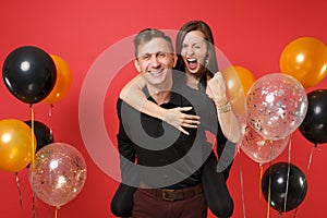 Stunning young couple in black clothes celebrating birthday holiday party on bright red background air balloons