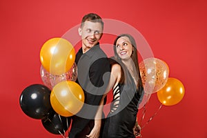 Stunning young couple in black clothes celebrating birthday holiday party on bright red background air balloons