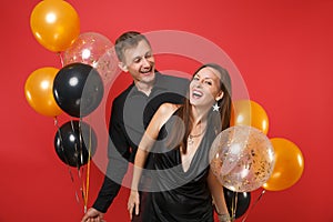 Stunning young couple in black clothes celebrating birthday holiday party on bright red background air balloons