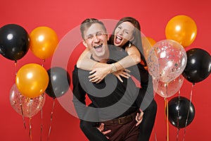 Stunning young couple in black clothes celebrating birthday holiday party on bright red background air balloons